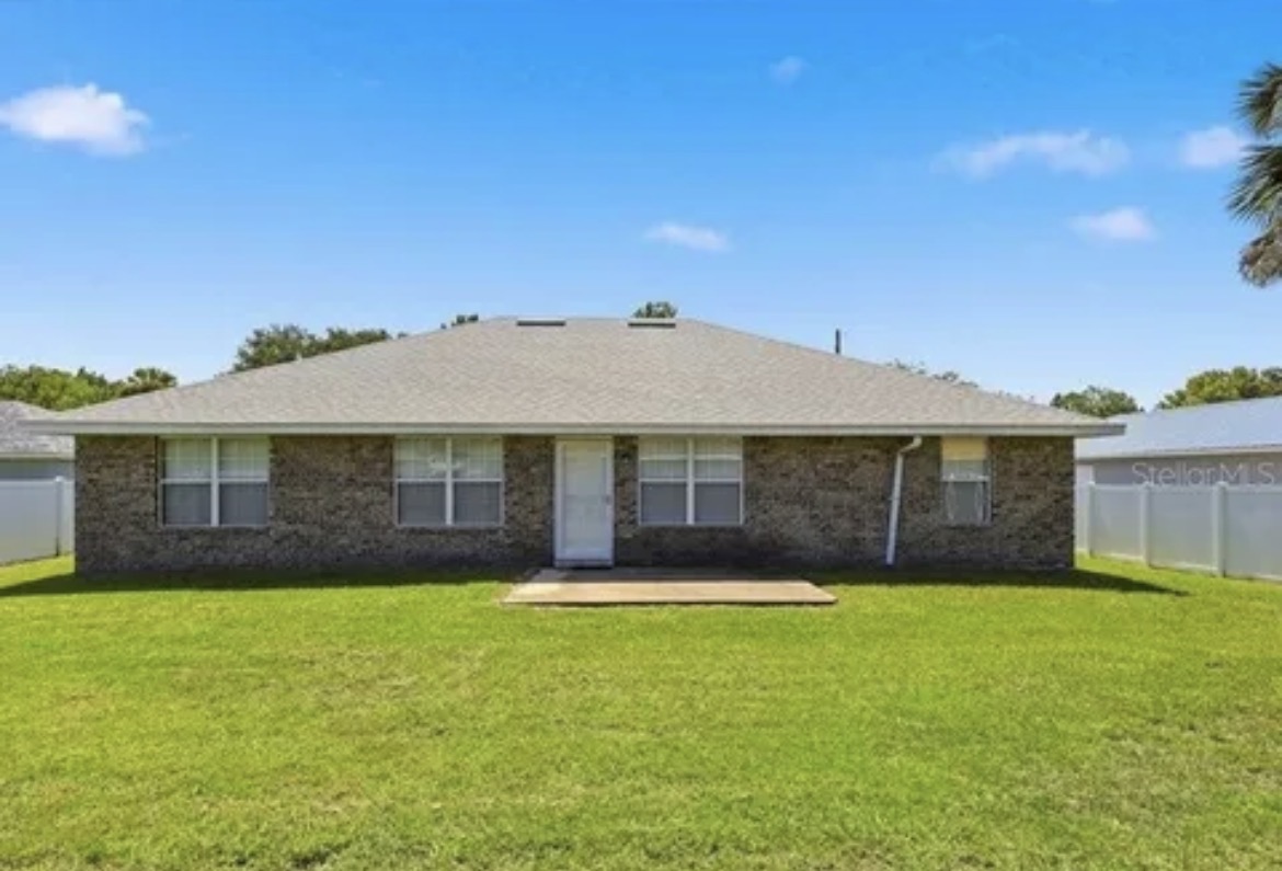 Rear exterior of the same TREV brick ranch home with a fenced backyard, patio, and generous green space